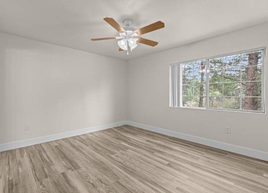 A room with a ceiling fan and a window with a view of trees.