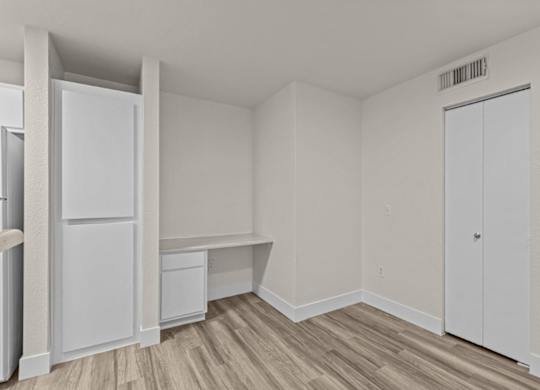 A white refrigerator is in a room with a wooden floor and white walls.