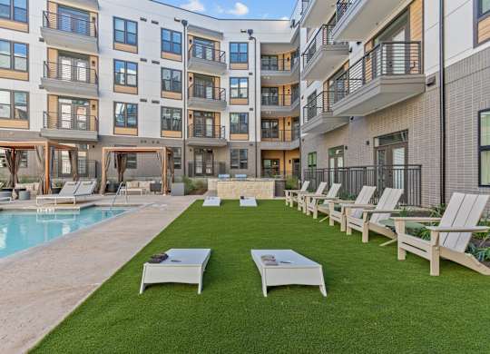 A large apartment complex with a pool and lawn chairs.