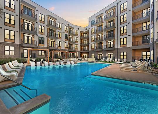 A large swimming pool surrounded by lounge chairs and buildings.