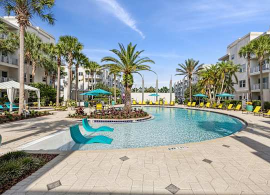 A pool surrounded by palm trees and lounge chairs.