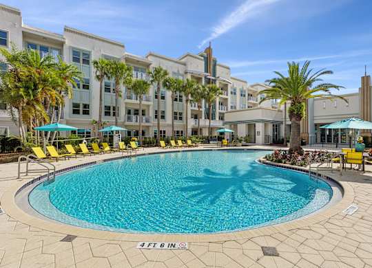 A large swimming pool surrounded by yellow chairs and palm trees.