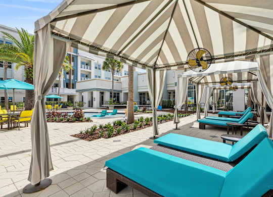 A sunny day at the pool with a striped umbrella providing shade.