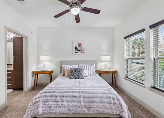 A bedroom with a bed, two lamps, and a ceiling fan.