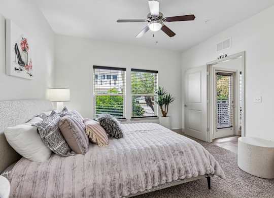 A bedroom with a bed, a ceiling fan, and a window with blinds.