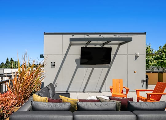 A modern outdoor seating area with a grey couch, orange chairs, and a grey sofa.