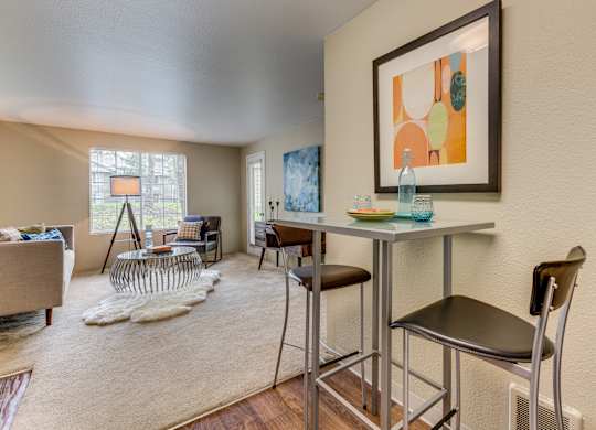 A living room with a grey sofa, a white rug, a glass table and a painting on the wall.