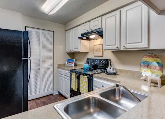 A black fridge sits in a kitchen with white cabinets and a stove.