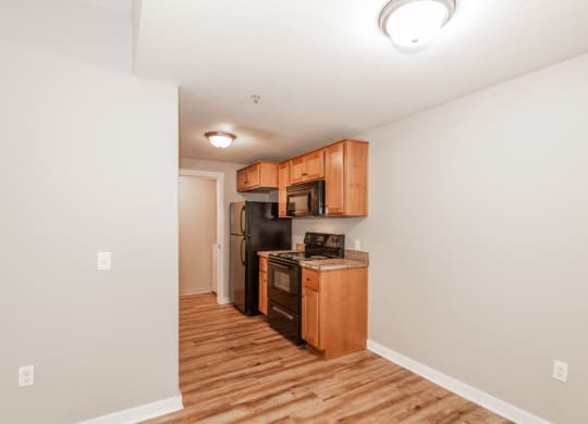 a kitchen with wood flooring and wooden cabinets and a black refrigerator