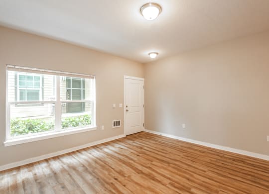 an empty living room with a large window and wood flooring