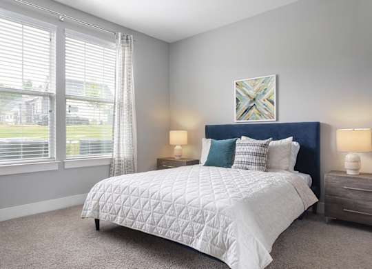 A bedroom with a large bed, two lamps, and a painting on the wall.