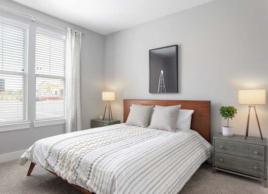 A bedroom with a bed, nightstand, and a window with blinds.