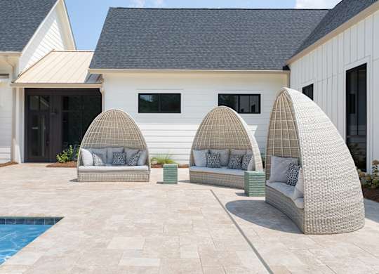 A white house with a pool and three wicker chairs.