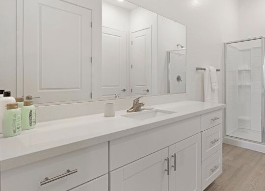 A white bathroom with a sink, mirror, and shower.