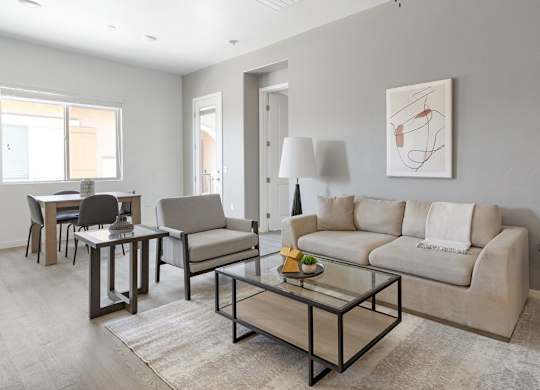 A modern living room with a glass coffee table and a beige sofa.