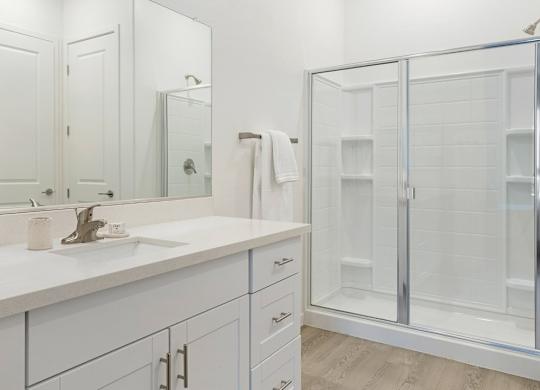 A white bathroom with a sink, mirror, and shower.