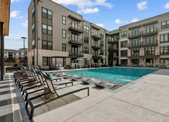 a swimming pool with chairs in front of an apartment building
