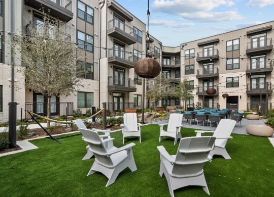 an outdoor lounge area with chairs and tables in front of an apartment building