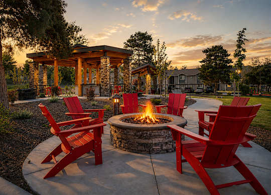 A fire pit surrounded by red chairs in a garden.