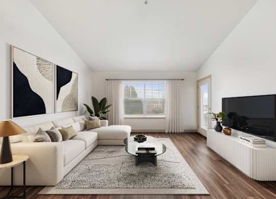 A modern living room with a white sofa, a coffee table, a large painting, a flat screen TV, and a window with curtains.
