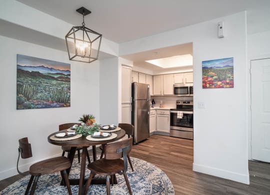 a dining area with a small table and chairs and a kitchen in the background