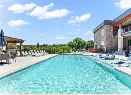 A large swimming pool with lounge chairs and umbrellas in front of a building.