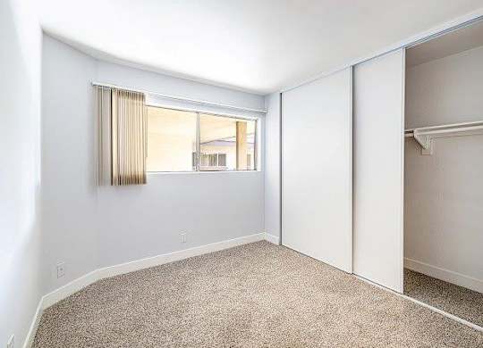 A room with a carpeted floor and a window with blinds.