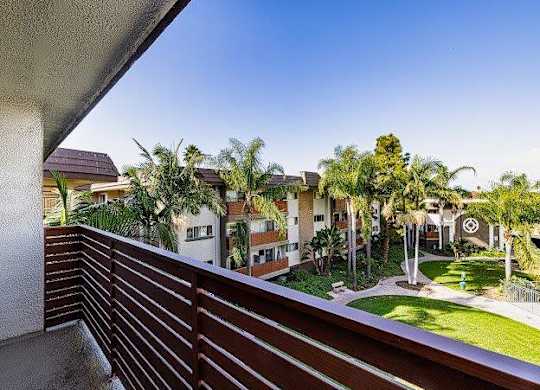 A balcony with a wooden railing overlooks a residential area with houses and palm trees.