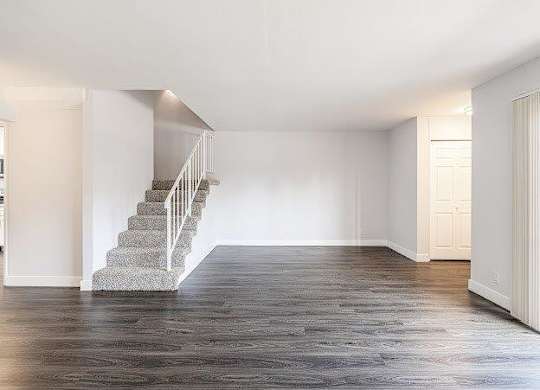 A spacious room with a staircase and wooden flooring.