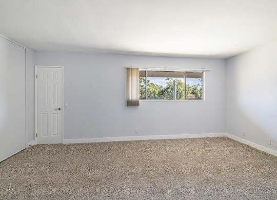 A room with a door and a window with a view of trees outside.