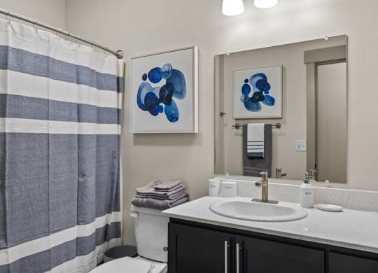 A bathroom with a striped shower curtain and two blue abstract paintings on the wall.