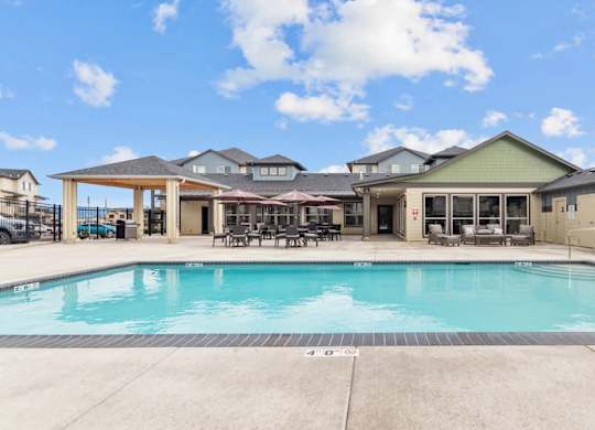 A large swimming pool in front of a building with a covered patio area.