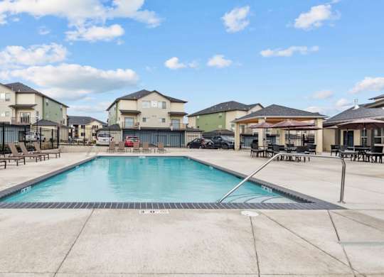 A swimming pool surrounded by lounge chairs and buildings in the background.