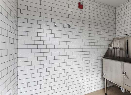 A white tiled wall with a red fire alarm on it.