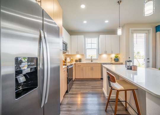 A modern kitchen with a stainless steel refrigerator and wooden flooring.