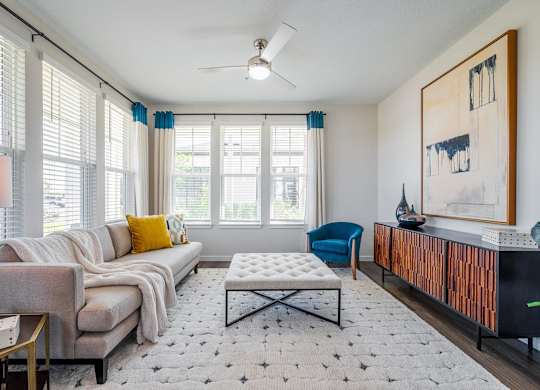 A living room with a grey couch, a blue chair, a white coffee table, and a painting on the wall.