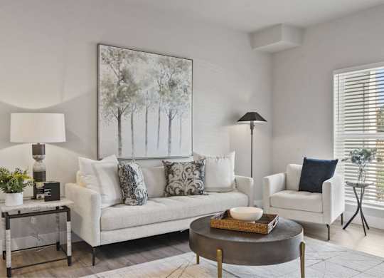 A living room with a white couch, a coffee table, and a painting on the wall.