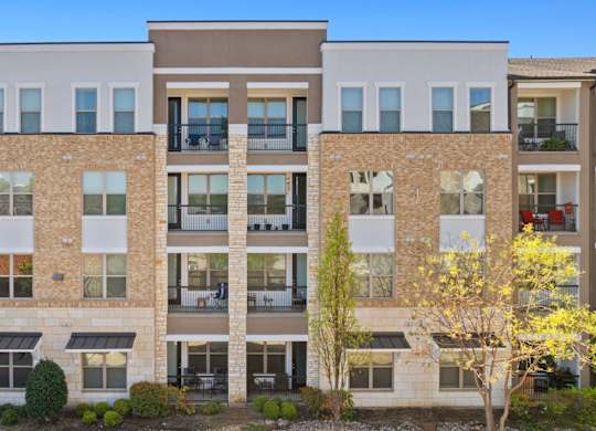 A row of apartment buildings with balconies and trees in front.