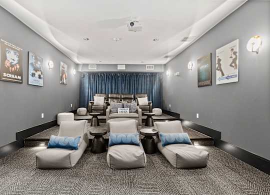 A room with grey walls and a carpeted floor has a row of white chairs with blue pillows.