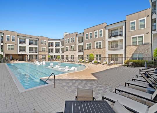 A swimming pool surrounded by apartment buildings and lounge chairs.
