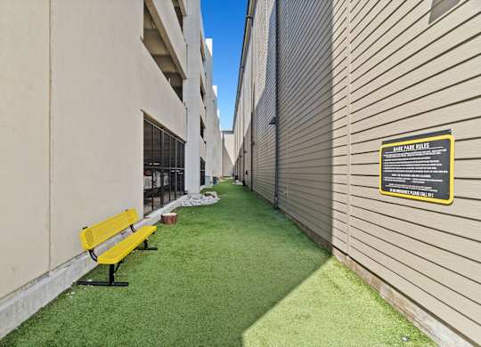 A yellow bench sits on a green lawn next to a building.