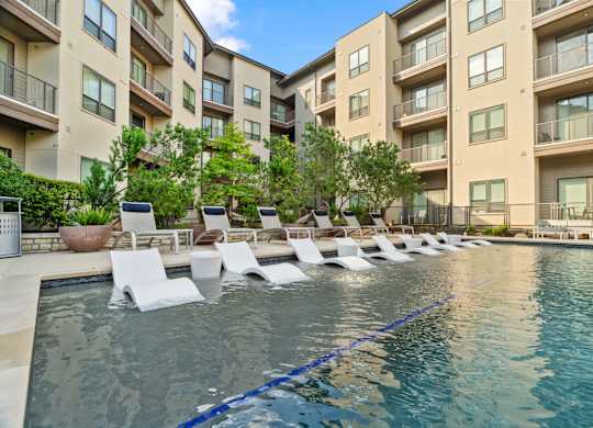 A pool with lounge chairs in front of apartment buildings.