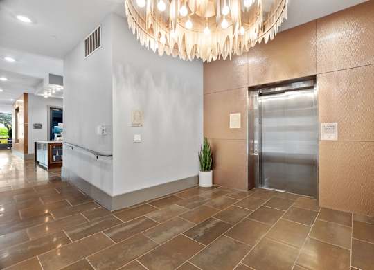 A large, modern chandelier hangs over a reception desk in a well-lit hallway.