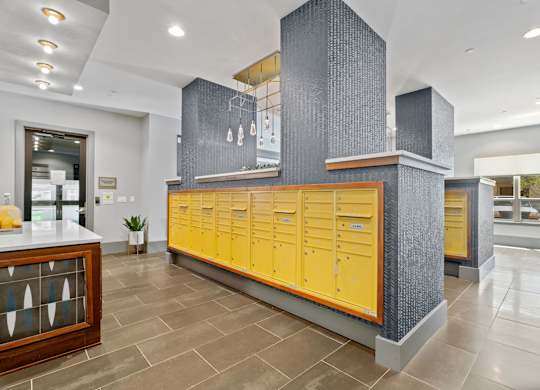 A row of yellow lockers are in a room with a grey column and a counter.