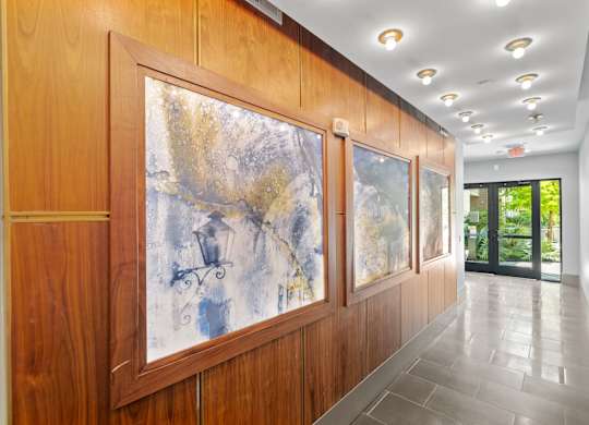 A hallway with a large painting on the wall and a glass door at the end.