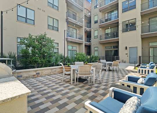 A patio with chairs and tables is surrounded by apartment buildings.