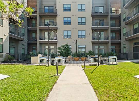 A concrete walkway leads to a grassy area with benches in front of apartment buildings.