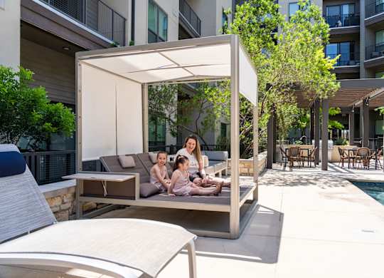 A woman and two children are sitting on a couch under a canopy on a patio.