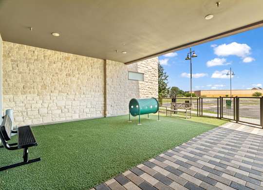 A patio area with a bench, a green trash can, and a brick wall.