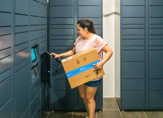 A woman is using a self-service machine with a package.